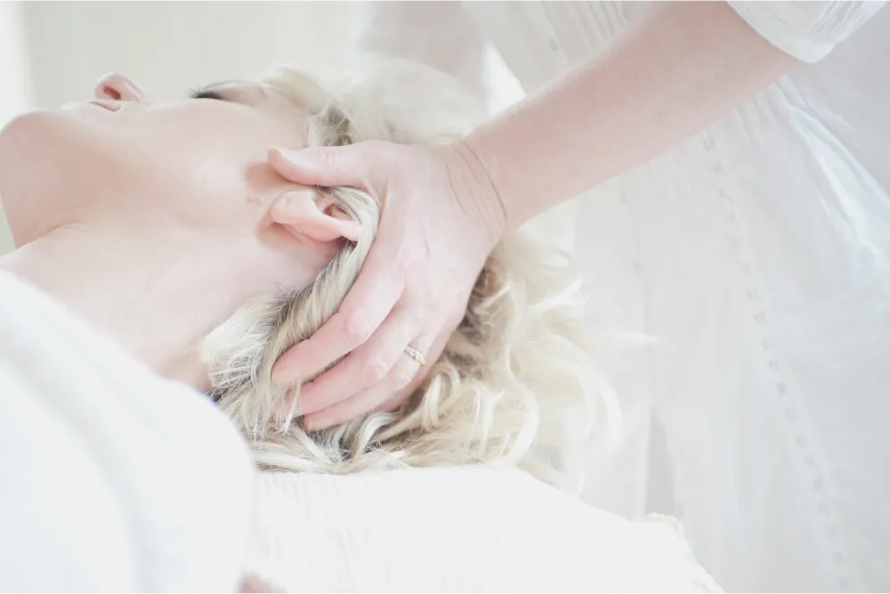 A woman receiving massage therapy on her neck. She is laying on a table with her head facing the left.
