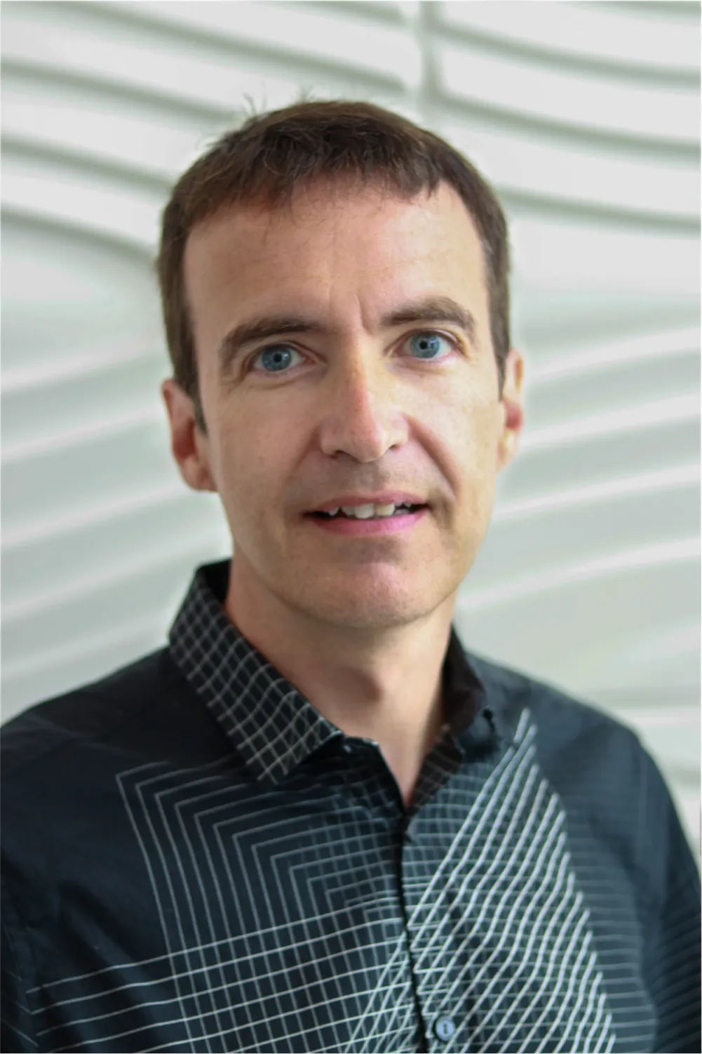 A profile picture of Dr. Duane Hartley in front of a white wall with a raised wave pattern.