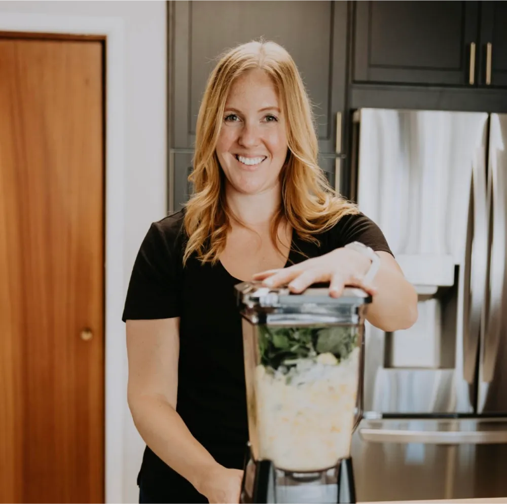 Photo of Stephanie Hnatiuk the Prota Clinic dietitian facing the camera in a kitchen with a blender on the counter.